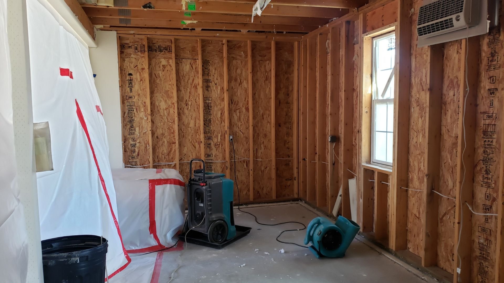 Interior room under construction with exposed wood framing and industrial fans